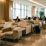 Intérieur d’un salon d’aéroport premium en correspondance, ambiance calme : sièges confortables, voyageurs avec bagages à main, éclairage doux et décor moderne.