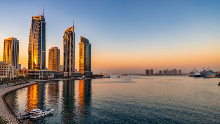 Vue panoramique de Manama au coucher du soleil, avec la baie calme, les gratte-ciel modernes illuminés et une atmosphère élégante au Bahreïn.